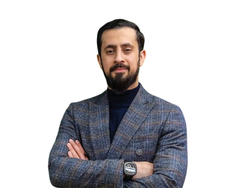 Portrait of Mehmet Yıldız with a short beard, wearing a plaid blazer over a dark turtleneck and a wristwatch, standing with his arms crossed on a transparent background.