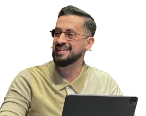 Headshot of Mehmet Yıldız, smiling and wearing glasses and a two-toned light beige polo shirt, working with a tablet in the foreground, on a transparent background.