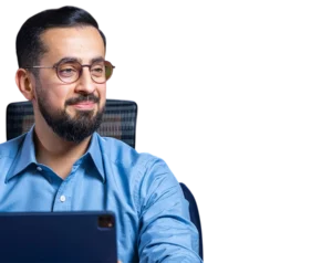 Headshot of Mehmet Yıldız, a Turkish speaker and founder of Hayalhanem, wearing a blue shirt and round glasses, looking to the side while working on a laptop.