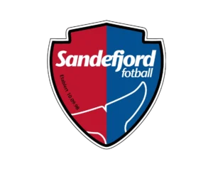 Sandefjord Fotball Club Logo, Shield-Shaped, Left Half Red, Right Half Blue, Featuring "Sandefjord" and "fotball" Text at the Top, a Whale Tail Motif at the Bottom, and Establishment Date (10.09.98).